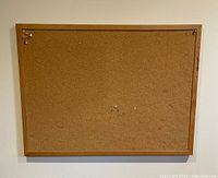 Small rectangular cork board with light wooden frame mounted on wall, showing cork surface with pinholes and minor discoloration.