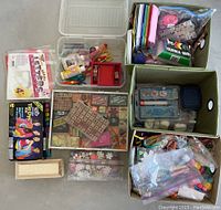 Overview of multiple craft supply containers filled with rubber stamps, glue, foam sheets, stickers, clay, and other art materials.