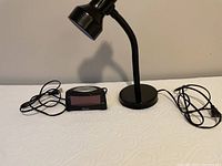 Black desk lamp with adjustable neck, power cord visible, and black digital alarm clock with red LED display.