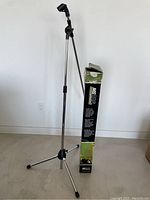 Full view of the assembled tripod boom microphone stand next to its original box showing stand height and design.