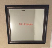 Full view of the square mirror showing its size and clear reflective surface with a dark wood frame.