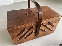 Photo of the sewing caddy closed showing its dark brown wood finish, central handle, and expandable multi-level side compartments.