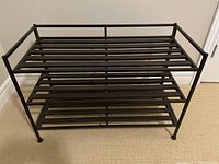Front view of black steel 3-tier shoe rack, showing slatted metal shelves and frame
