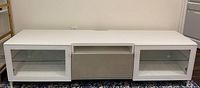 Front view of white IKEA entertainment stand showing two glass door cabinets and central drawer