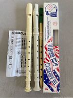 Two cream plastic recorders, green and brass American slide whistle in box with Suzuki instruction sheet, brass Irish whistle.