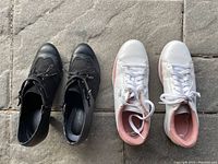 Top view of black dress booties next to white running shoes with pink accents on stone floor, showing condition and design details.