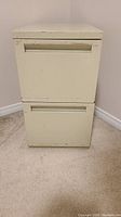 Front view of 2 drawer metal filing cabinet showing aged cream finish and recessed handles.