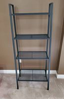 Front view of the black metal shelf showing all four mesh shelves and overall structure.