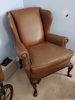 Brown high-back leather chair with visible shape and structure, wooden carved legs and nailhead trim