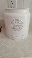 Front view of white ceramic canister with embossed 'Tools Bistro Utensils' label.