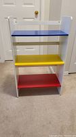 Front view of child's book/toy shelf with blue, yellow, and red shelves and white frame