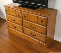 Front angle view of the dresser showing six drawers, warm maple finish, metal handles, and minor surface wear.
