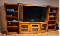 Full view of the oak 6-piece entertainment unit including bookcases flanking a central TV niche and bottom cabinets with glass doors.