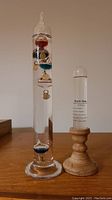 Front view of Galileo thermometer and storm glass on wooden stands showing colorful bulbs and clear liquid.