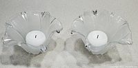 Top view of two clear and frosted glass floral candle holders each holding a small white candle.