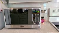 Front view of the stainless steel Panasonic microwave oven on kitchen counter showing control panel and digital clock display on.