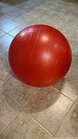 Red exercise ball on tiled floor showing overall condition and size reference.