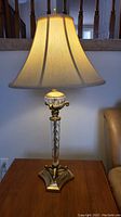 Tall table lamp with ornate brass base and large bell-shaped shade on a wooden table.