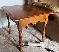 Side view of wooden side table showing scalloped skirt and turned legs, placed next to a couch.