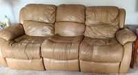 Front angled view of the tan leather 3-seat couch showing the worn right end and padded armrests with visible stitching.