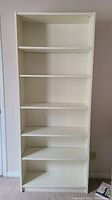 Full front view of white tall 6-shelf melamine bookcase against wall