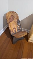 Angled front view of wooden chair showing carved elephant on backrest and seat.