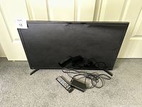 Samsung 32-inch TV with power cord and remote control placed on floor against door.