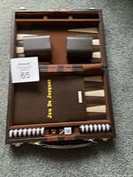Open backgammon set showing checkers, dice cups, doubling cube, and game board points inside brown case.