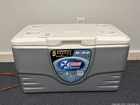 Closed gray and white Coleman Xtreme cooler showing front label and cup holders on lid.