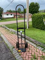 Front view of the black metal dolly with vertical handle and two large wheels.