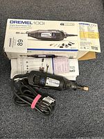 Dremel 100 rotary tool with power cord laid on floor next to original box and instruction papers