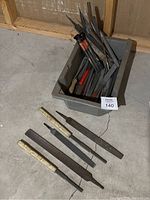 Large plastic bin containing assorted metal and woodworking files and rasps in different shapes and sizes, some with handles, some without, with visible wear and usage marks.