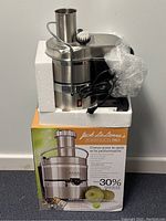 Jack LaLanne Power Juicer Pro juicer in original packaging with foam inserts, power cord wrapped, and cleaning brush on top.