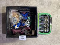 Top view of plastic crate containing various ratchet straps, chains, and metal hooks with new green ratchet strap set placed beside it