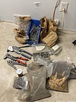 Lot overview showing various rivets in bags and containers along with rivet tools on concrete floor near a wall outlet.