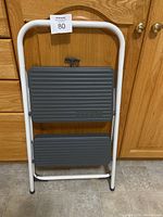 Front view of two-step stool with white metal frame and grey plastic steps.