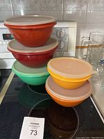 Five stackable vintage Tupperware bowls with lids in various colors arranged on a stovetop.