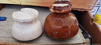 Photo showing side view of two antique glass telephone pole insulators on wooden surface, one brown and one cream, with visible chips on bottom edges