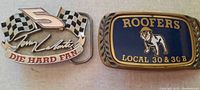 Photo showing two heavy belt buckles: a Die Hard Team #5 buckle with checkered flags and Tony Liberti autograph, and a Roofers Local 30 & 30B buckle with bulldog graphic on blue background.