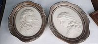 Two vintage framed oval ceramic art pieces with embossed Victorian style female profiles on white ceramic with bronze-toned oval frames.