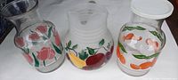 Three vintage glass beverage pitchers side by side showcasing their hand painted and applied label designs.