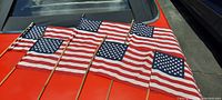 Six small American flags spread out displaying front side, showing stars and stripes clearly on an orange surface, mounted on wooden sticks.