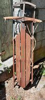 Front view of the antique Lightning Glider wooden sled showing the top handle and three vertical main base planks, alongside the attached rope and metal hardware beneath the wooden handle.