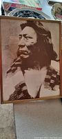 Framed sepia photograph of Native American man in traditional attire on beige surface.