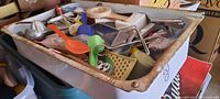 Wide view of large bin filled with various vintage kitchen utensils, showing general condition and assortment including scoops, graters, juicers, and measuring spoons.