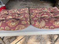 Front view of two large, tufted chair cushions with floral pattern on table.