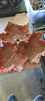 Photo showing top view of red and brown ceramic leaf-shaped sectioned serving dish with three sections and a central handle, placed on a surface.
