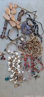 Overview of various vintage costume jewelry pieces laid out, showing peach-colored beaded necklace, goldtone heavy chain, multicolored bracelets, pearl string, earrings, and other chains.