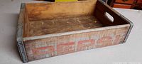 Side view of wooden Pepsi Cola crate showing worn red Pepsi lettering and metal corner clamps.
