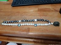 Full view of the grey and white baroque freshwater pearl necklace laid flat, showing the variation of pearl sizes and the attached carved Buddha head pendant.